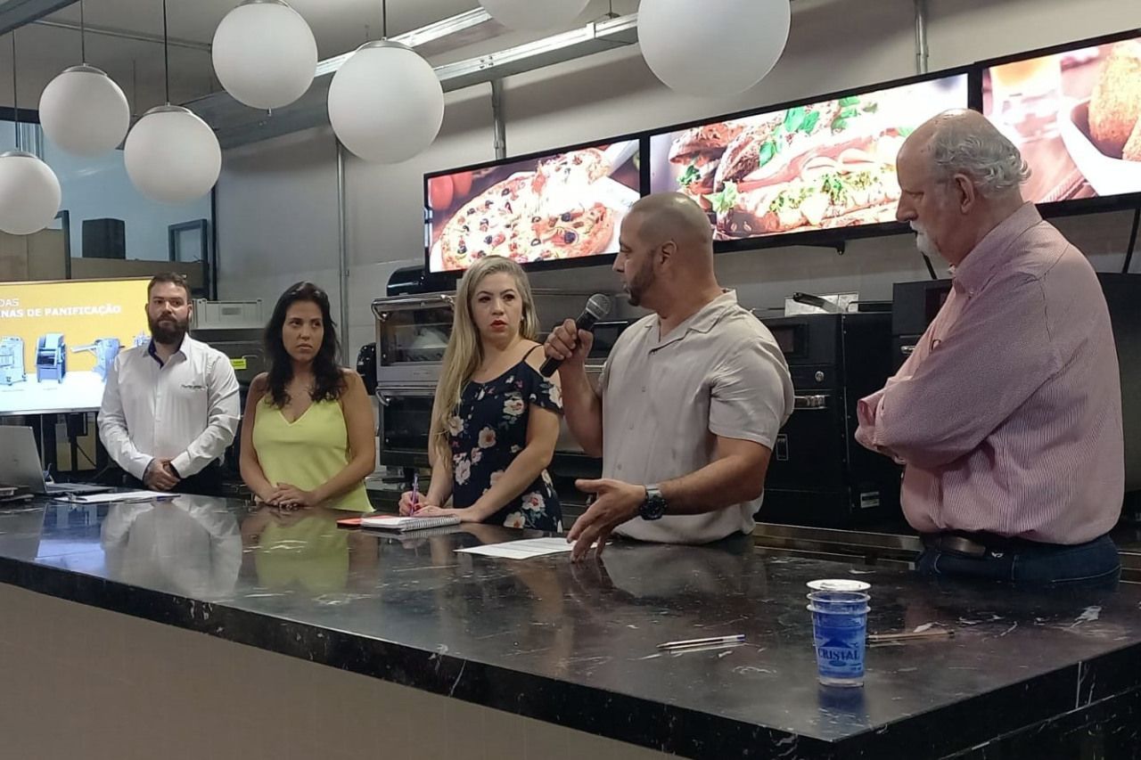 Um grupo de pessoas sentadas à mesa com um homem falando em um microfone