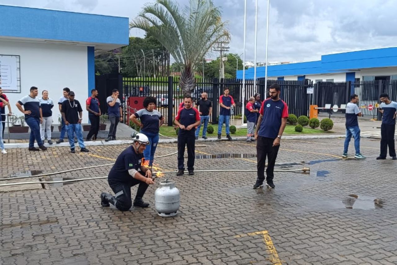 Grupo de pessoas assistindo a um homem demonstrando como extinguir um incêndio em um tanque de propano.