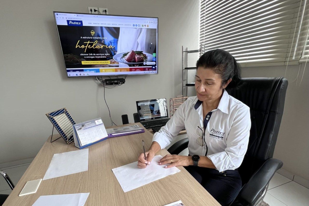 Uma mulher está sentada em uma mesa escrevendo em um pedaço de papel.