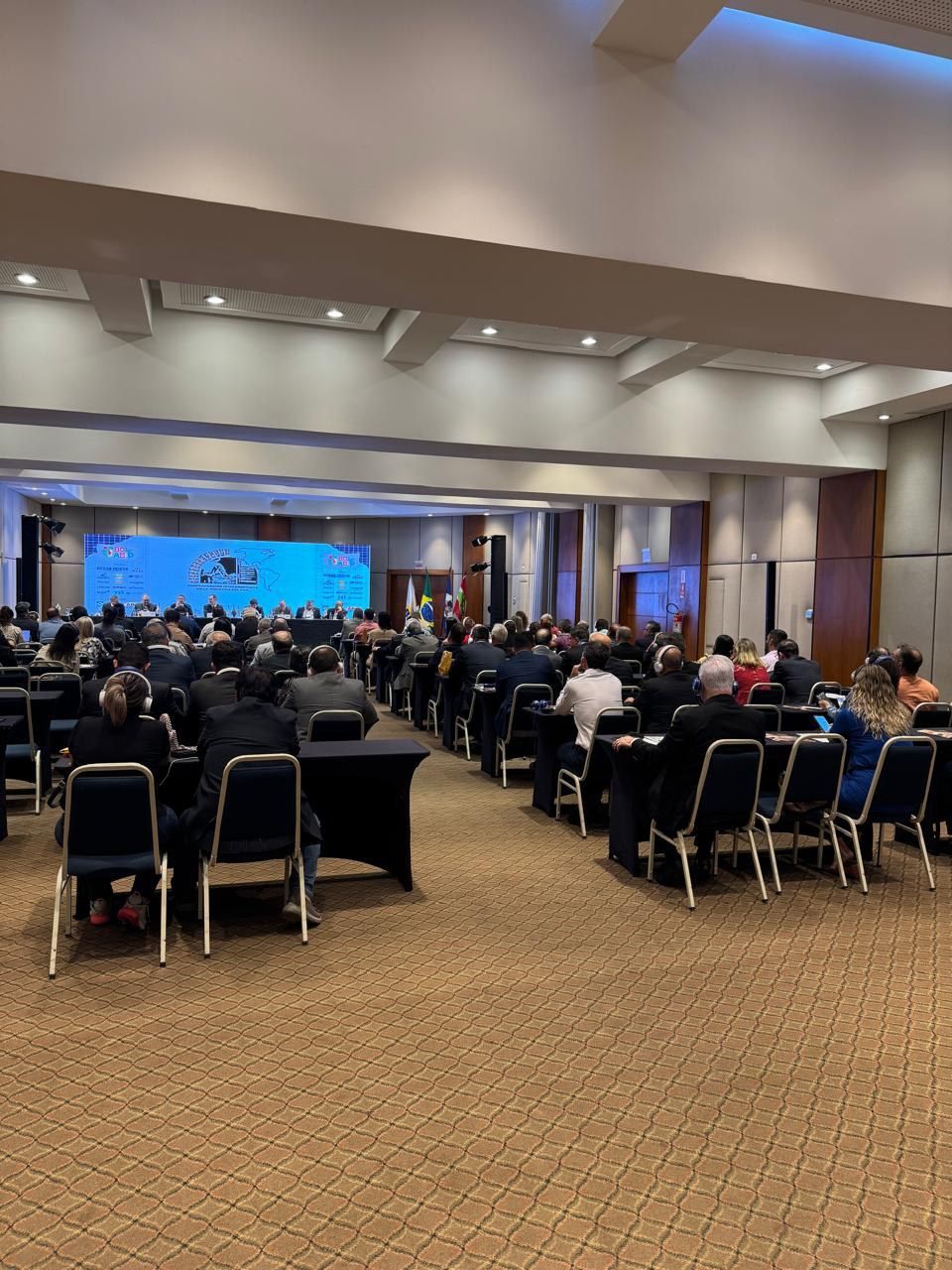 Uma grande sala cheia de pessoas sentadas em mesas e cadeiras.