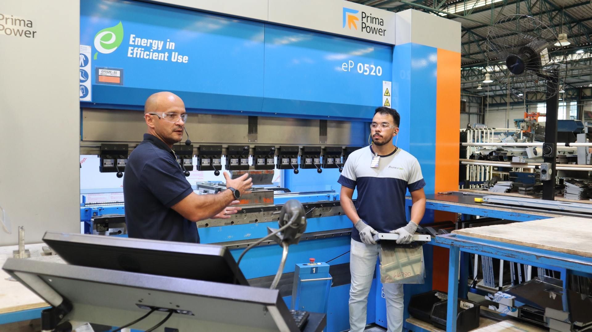 Dois homens estão parados em frente a uma máquina em uma fábrica.