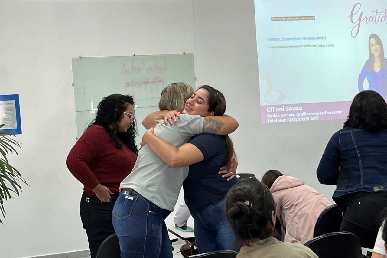 Um grupo de mulheres se abraçam em frente a uma tela de projetor.