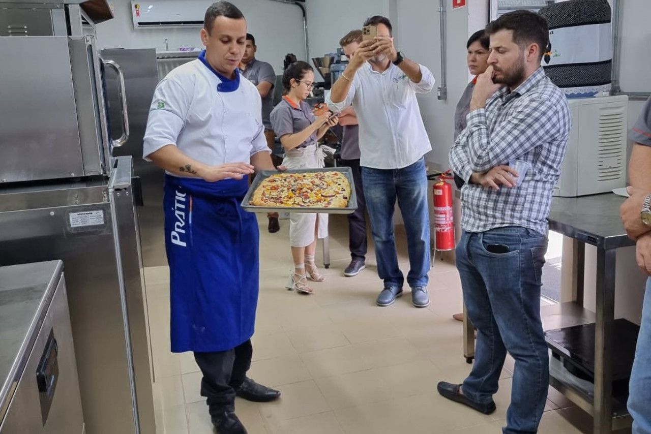 Um homem de avental azul está segurando uma bandeja de pizza em uma cozinha.