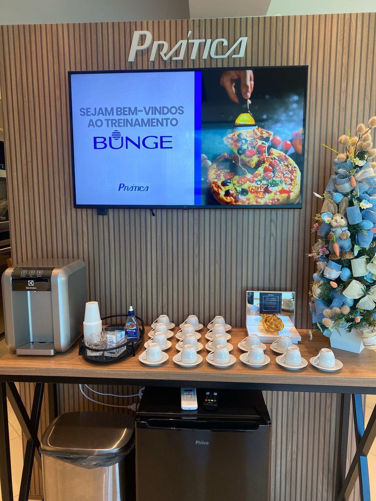 Há uma mesa com xícaras e uma TV na parede.