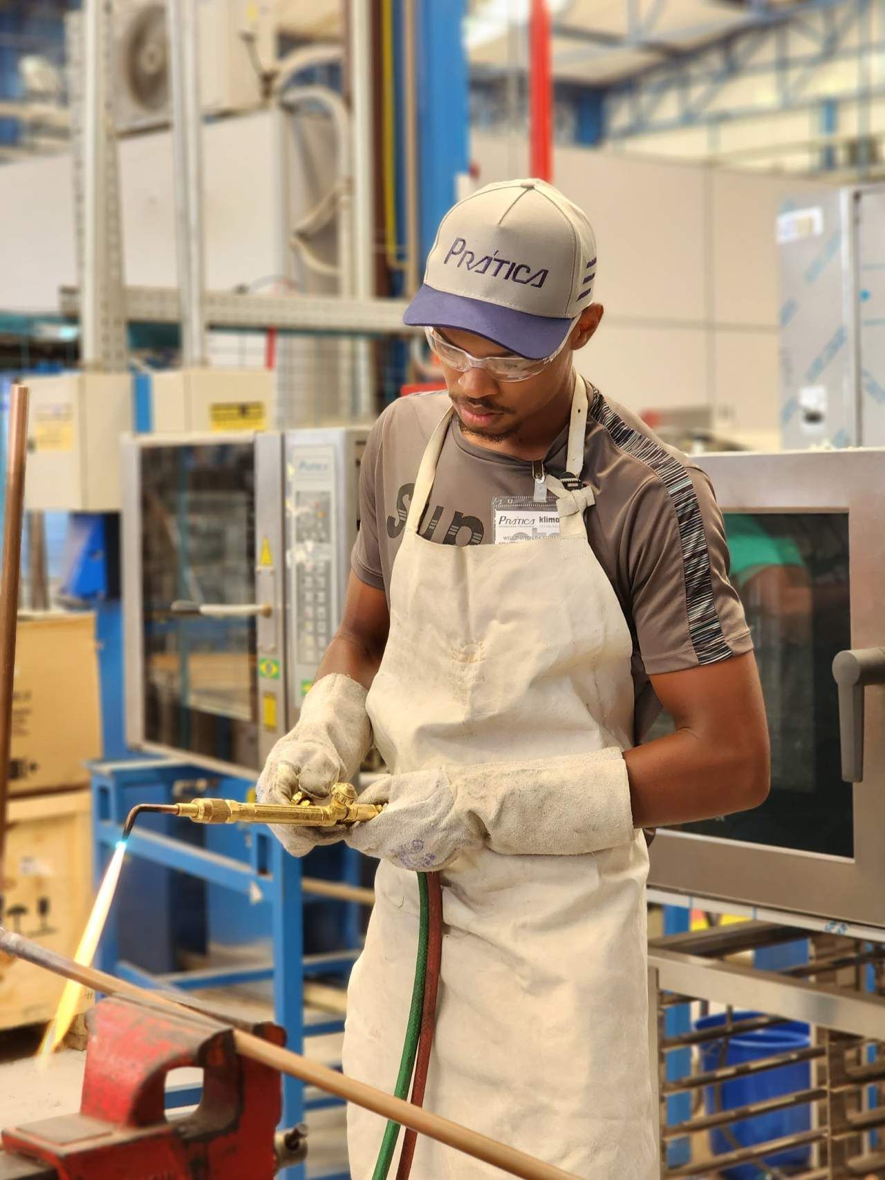 Um homem vestindo avental e luvas está trabalhando em uma fábrica.