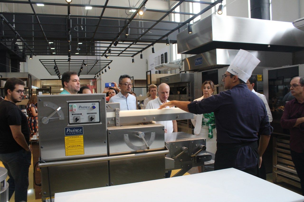 Um homem com chapéu de chef está conversando com um grupo de pessoas em uma cozinha