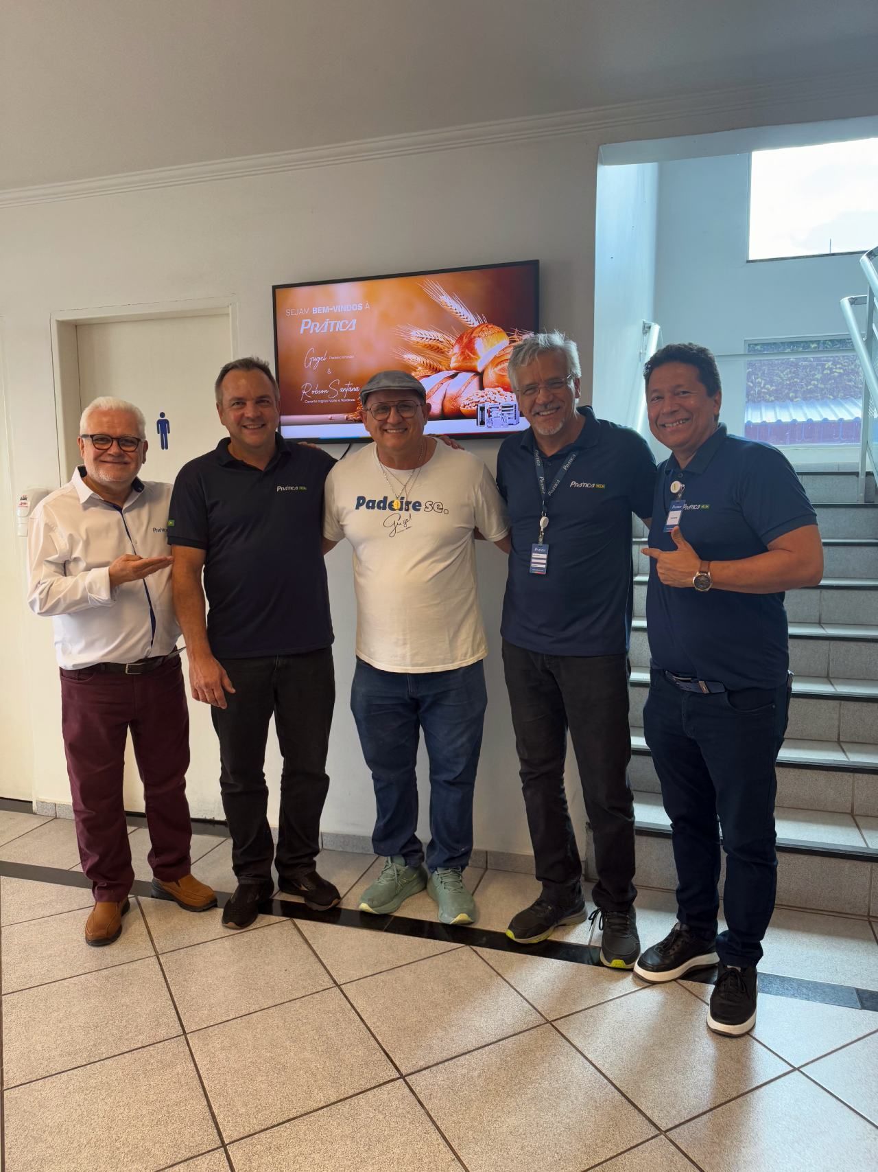 Um grupo de homens está posando para uma foto em frente a uma televisão.