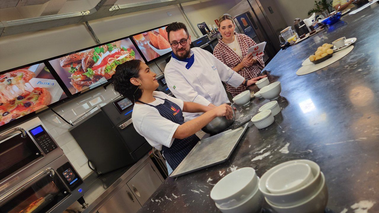Um grupo de pessoas está em pé ao redor de uma mesa em uma cozinha preparando comida.