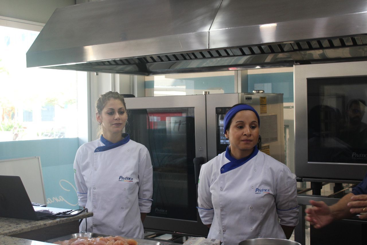 Duas mulheres em jalecos brancos de chef estão em uma cozinha