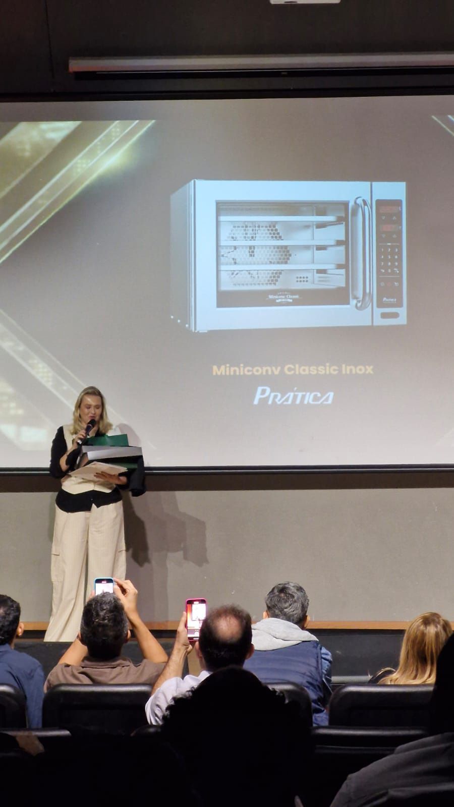 Uma mulher está fazendo uma apresentação em frente a uma tela grande.