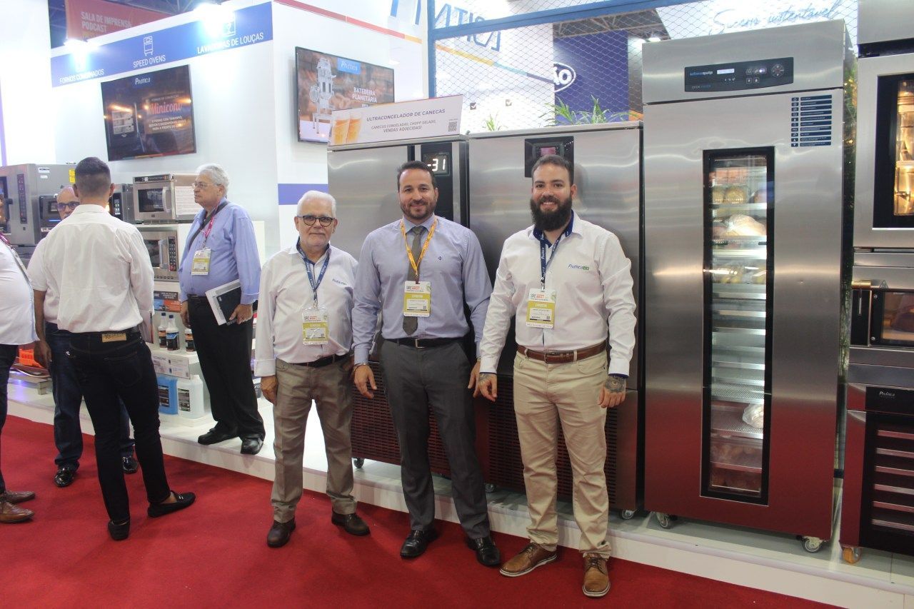 Um grupo de homens está parado um ao lado do outro em frente a uma geladeira.