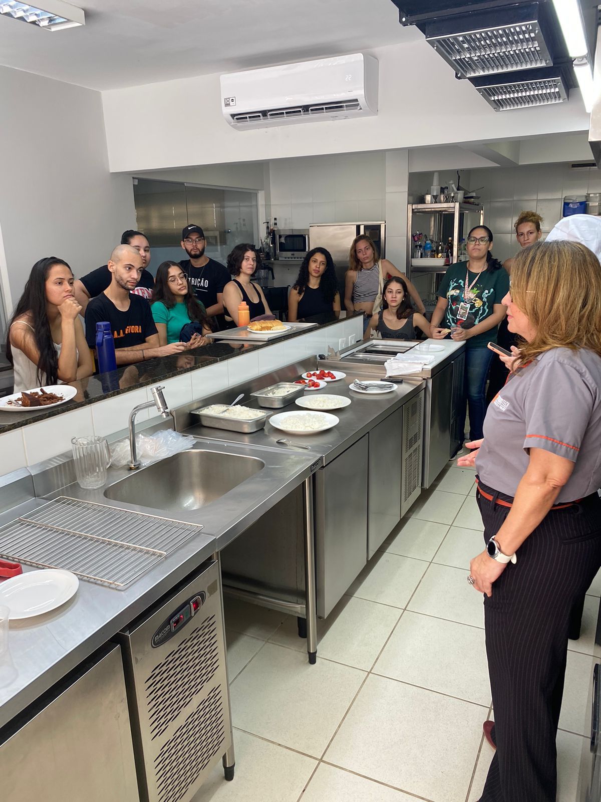 Um grupo de pessoas está de pé ao redor de um longo balcão em uma cozinha.