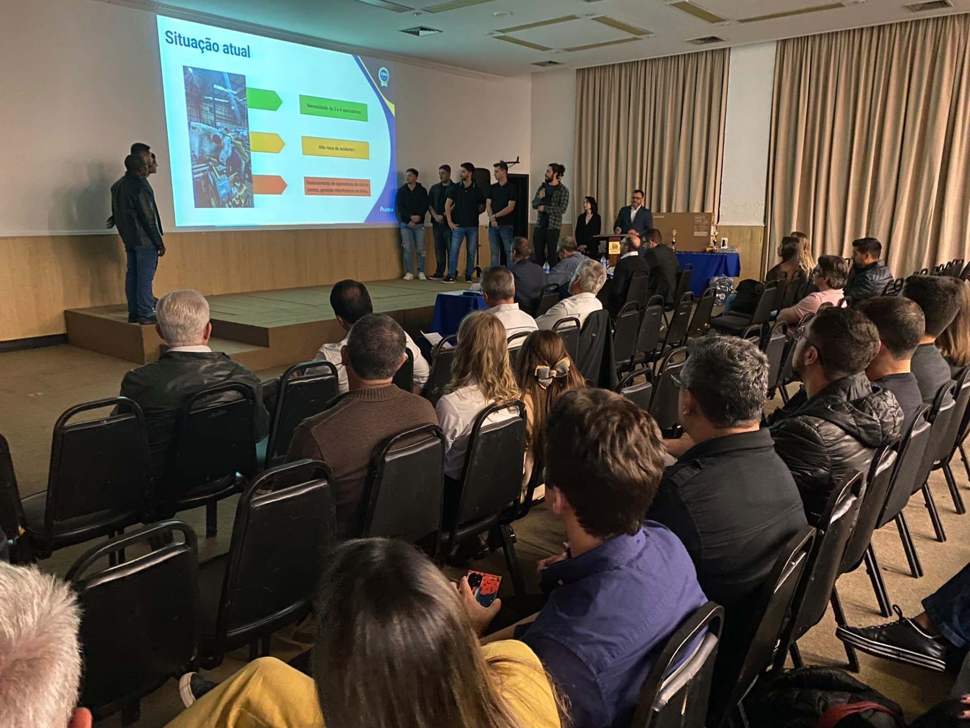 Um grupo de pessoas está sentado em cadeiras em frente a uma tela de projetor.