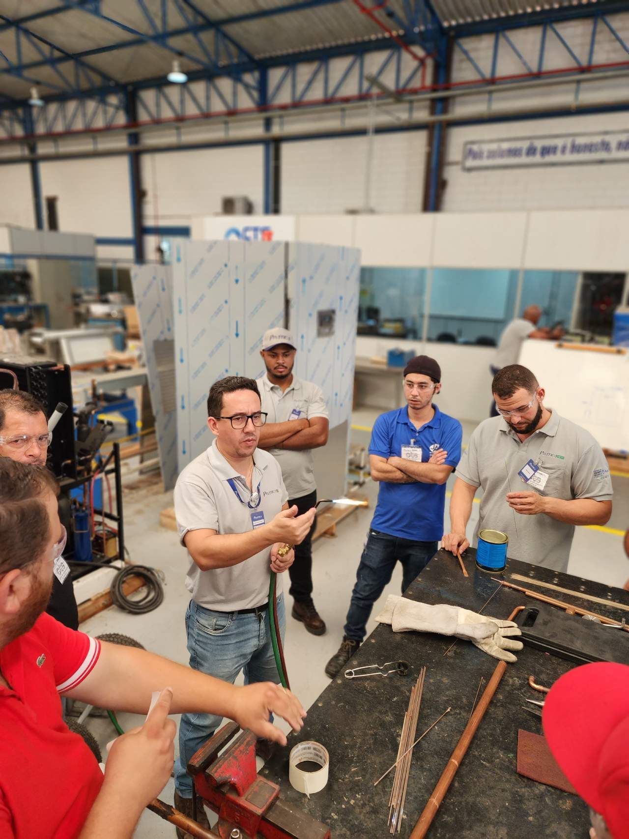 Um grupo de homens está em volta de uma mesa em uma fábrica.