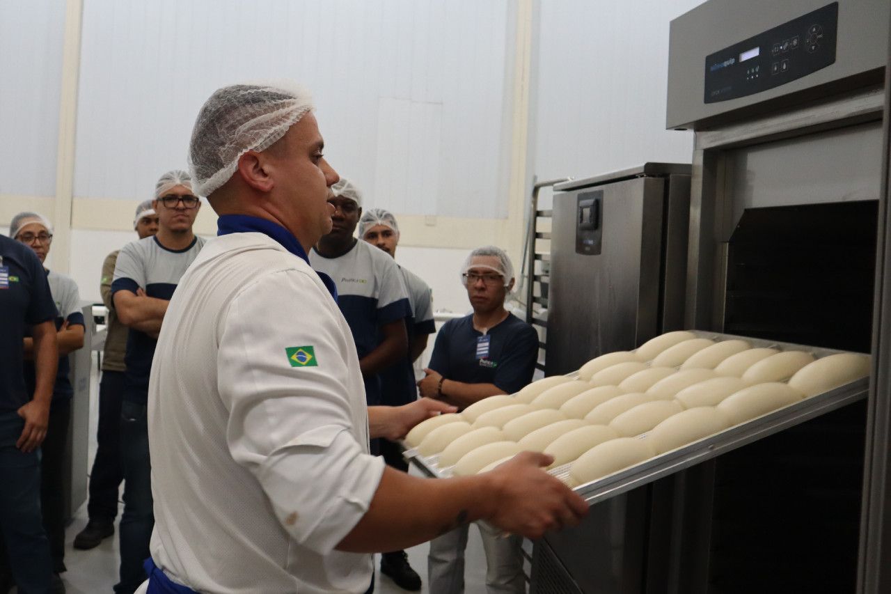 Um homem está segurando uma bandeja de massa em frente a um forno.