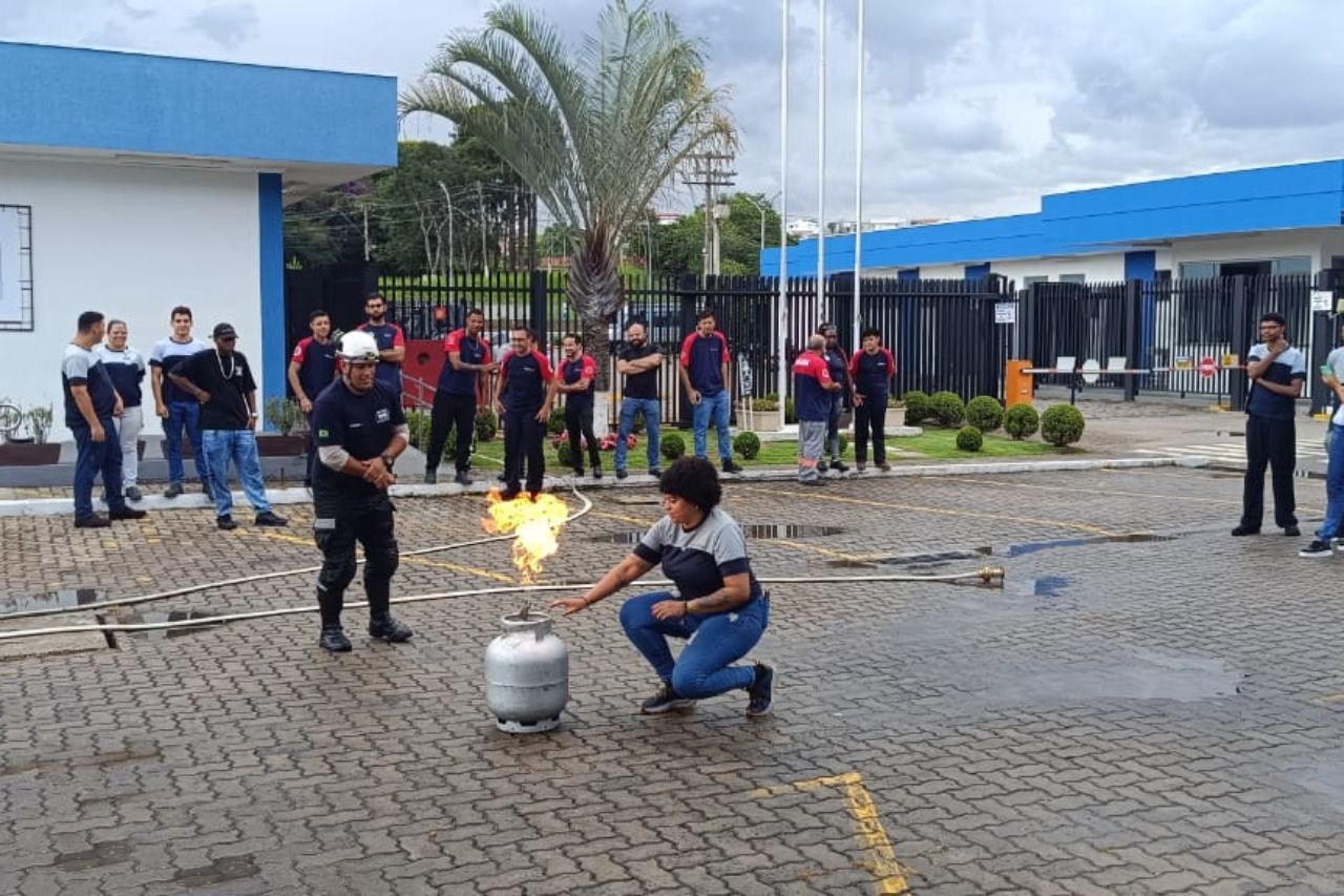 Treinamento de segurança contra incêndio; pessoa apagando gás de um tanque de propano na presença de espectadores.