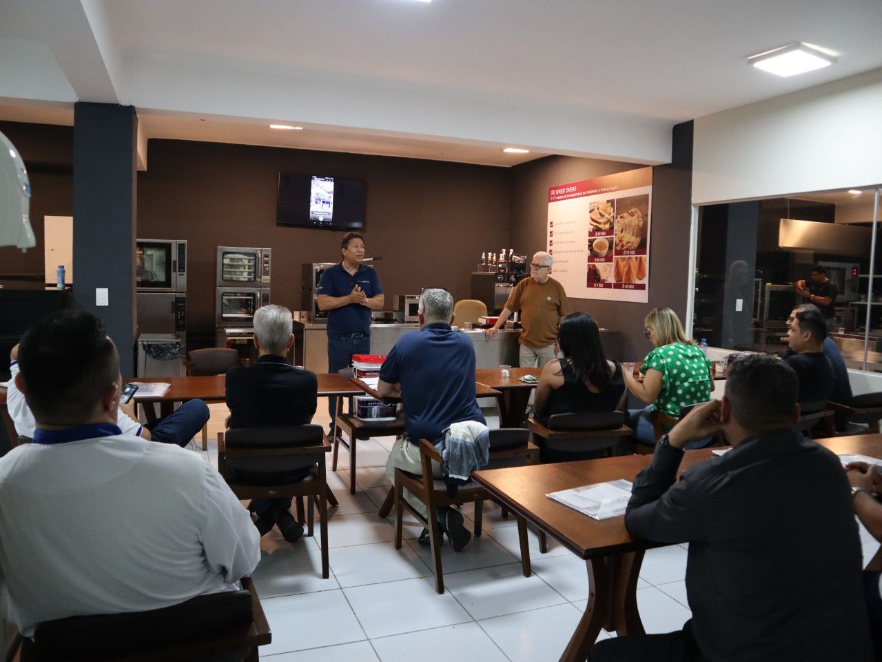 Um grupo de pessoas está sentado em mesas em uma sala.