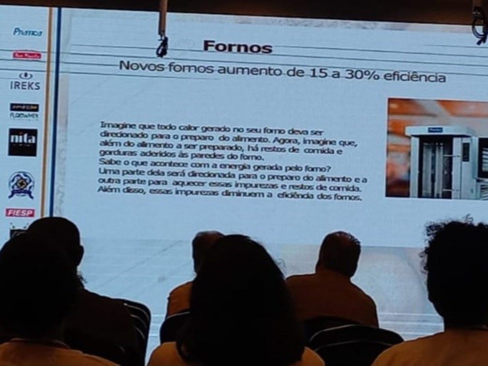 Um grupo de pessoas está sentado em frente a uma tela grande que diz fornos