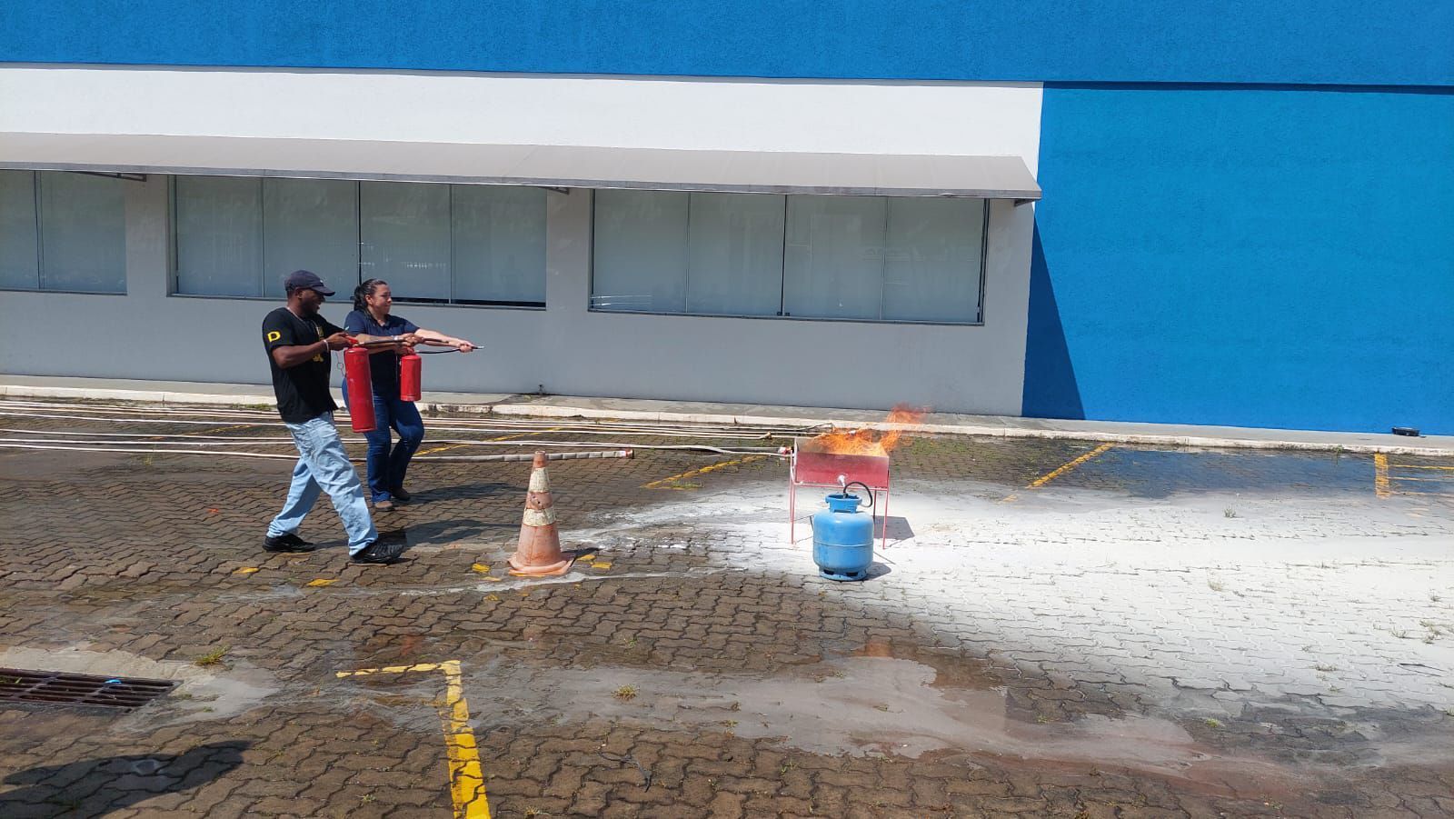 Dois homens estão parados em frente a um prédio azul segurando um extintor de incêndio.