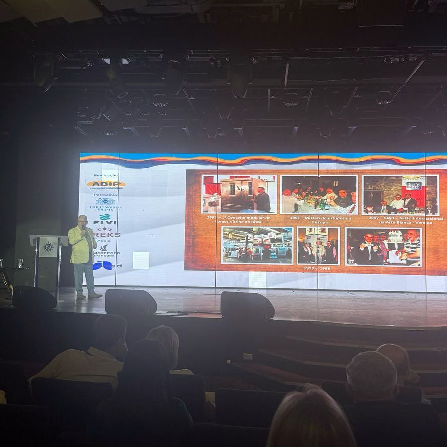 Um homem está fazendo uma apresentação em um palco em frente a uma tela grande.