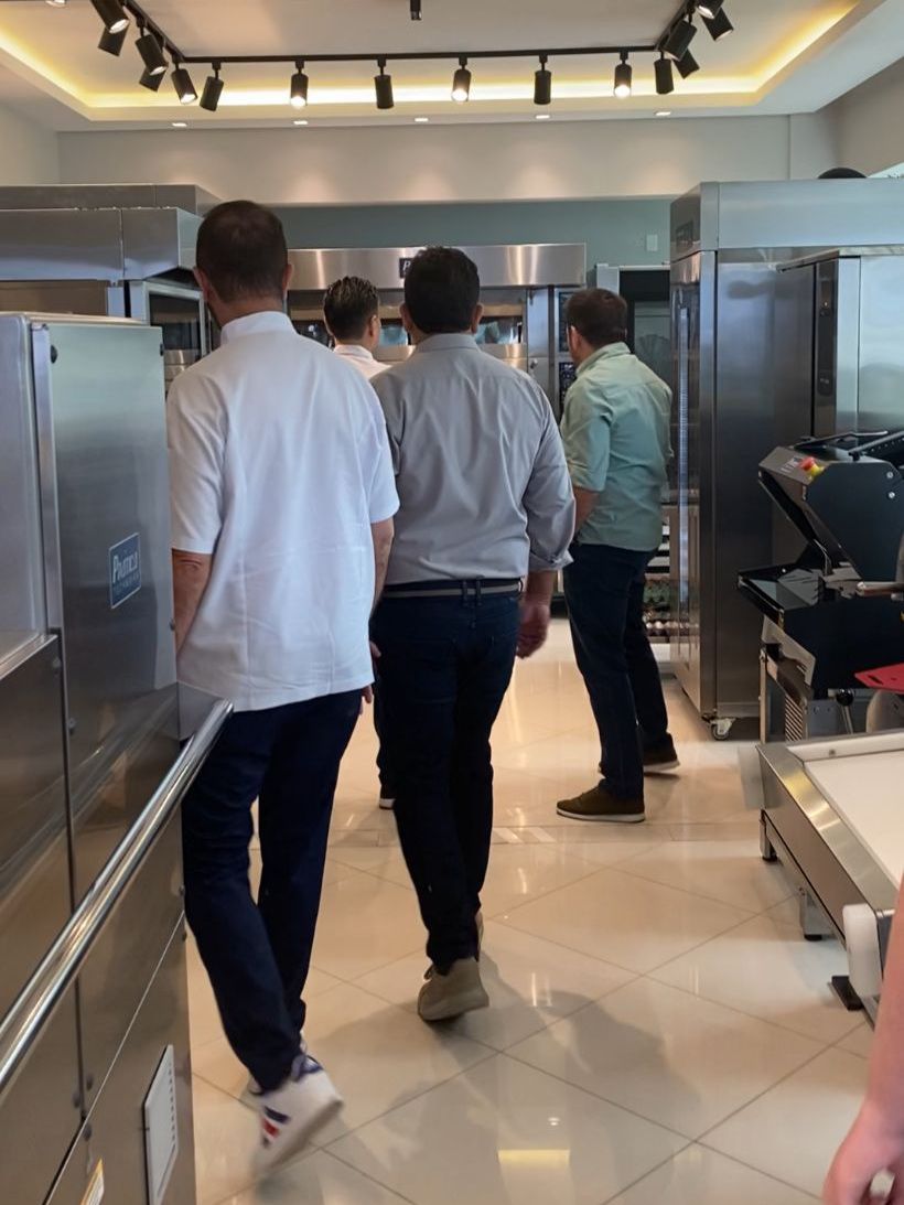 Um grupo de homens está caminhando por uma cozinha com eletrodomésticos de aço inoxidável