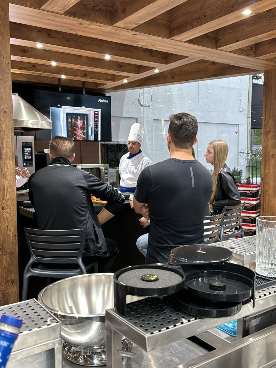Um grupo de pessoas está sentado à mesa de uma cozinha conversando com um chef.