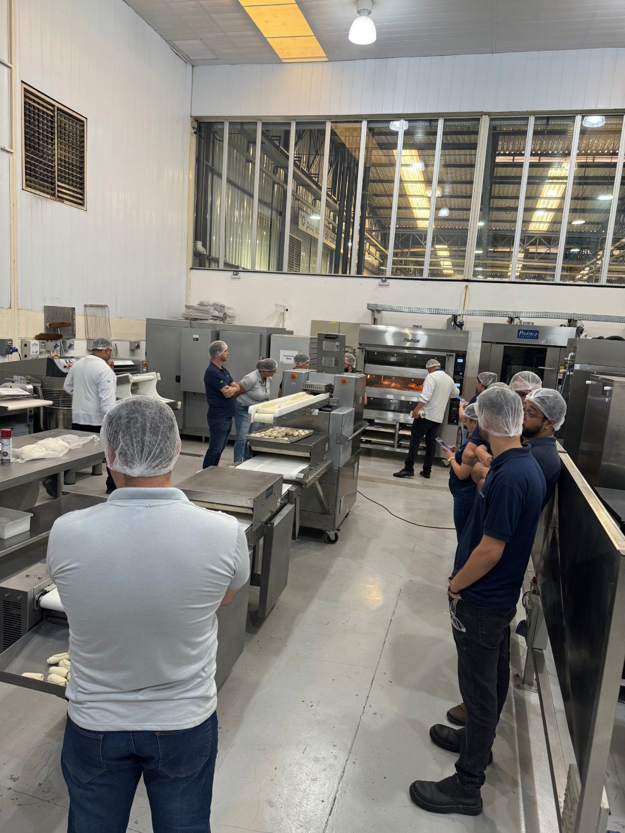 Um grupo de homens está em uma padaria olhando para uma máquina.