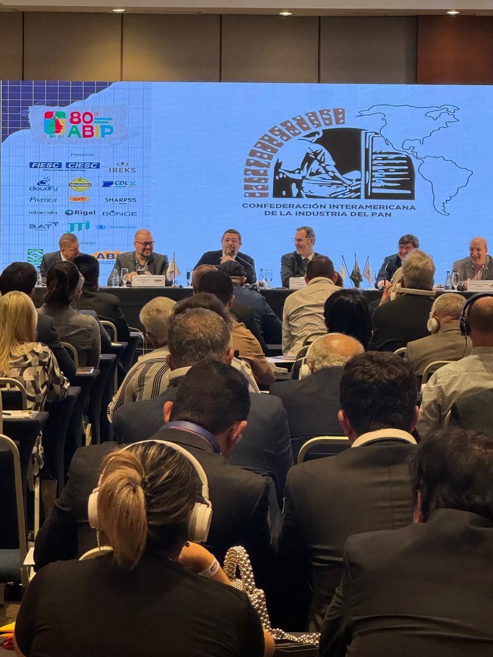 Um grande grupo de pessoas está sentado em frente a uma tela grande.