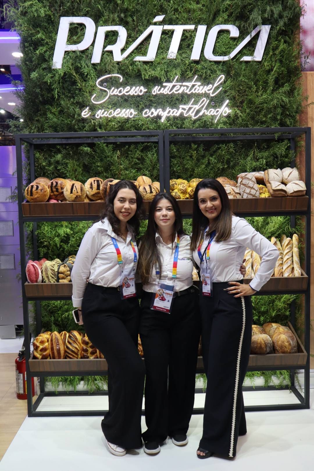 Três mulheres estão posando para uma foto em frente a uma exposição de frutas e vegetais.