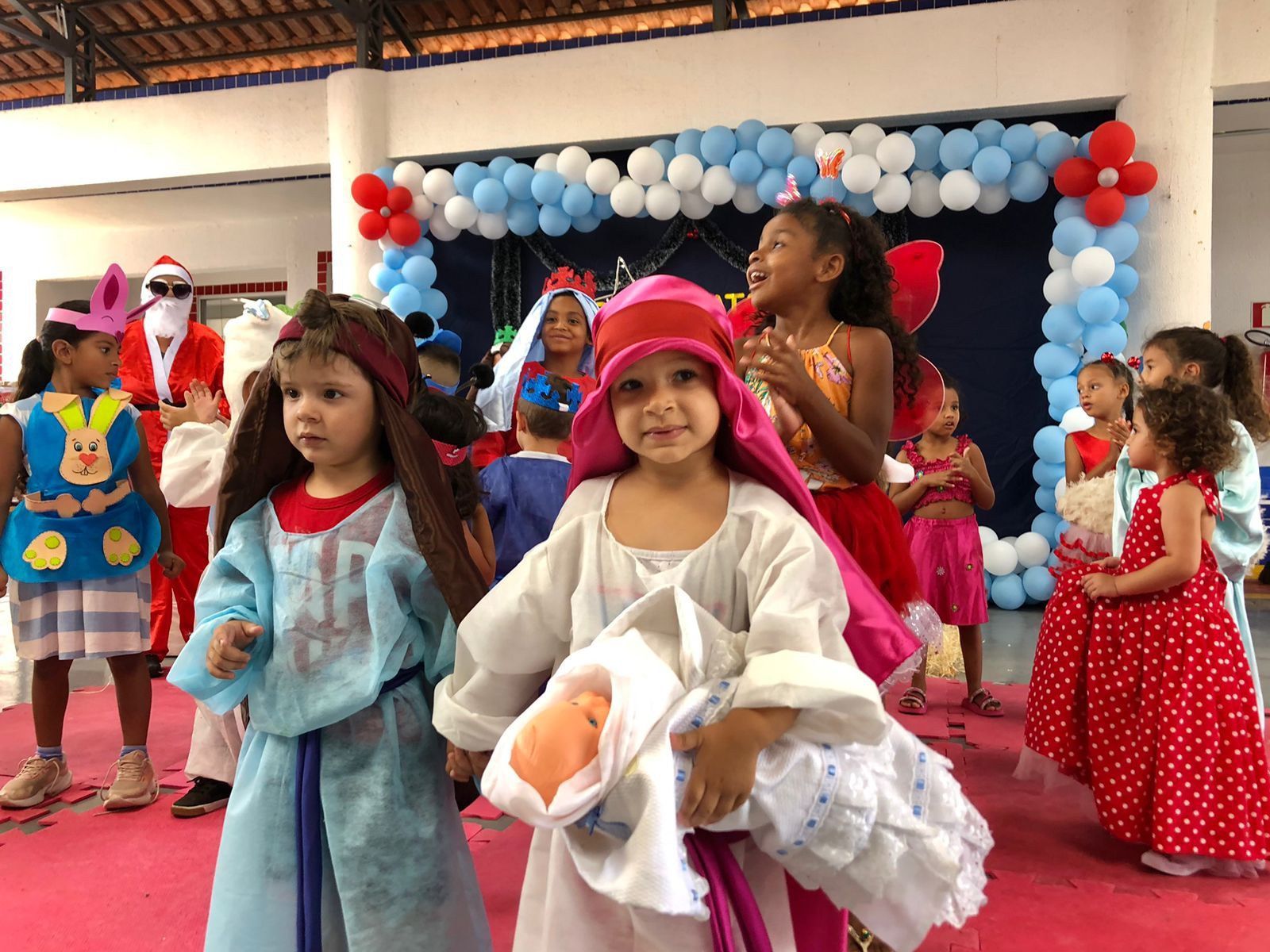 Um grupo de crianças fantasiadas dançam em uma sala com balões.