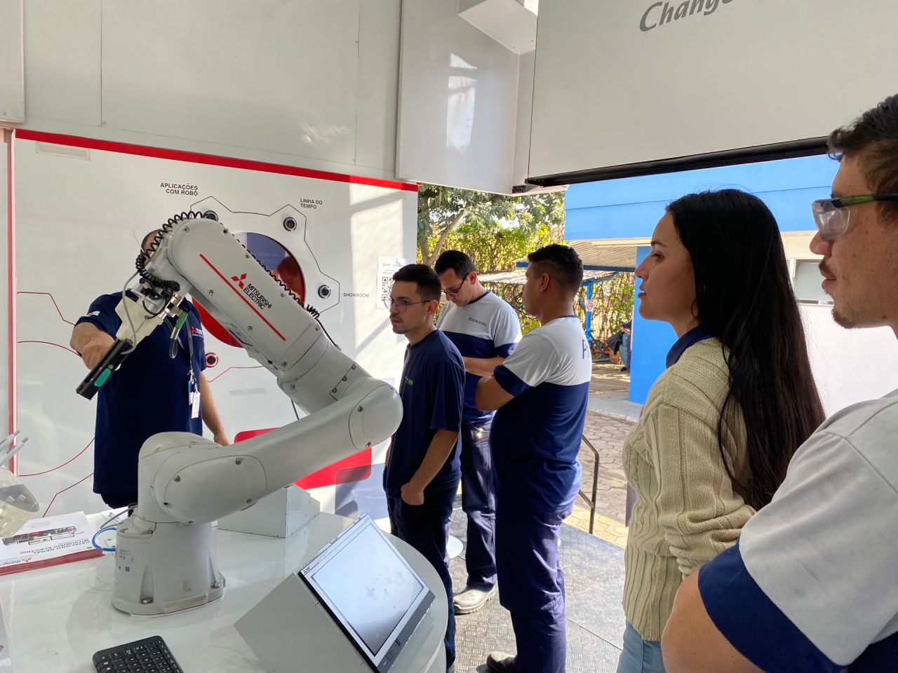 Um grupo de pessoas está em pé ao redor de um braço robótico.