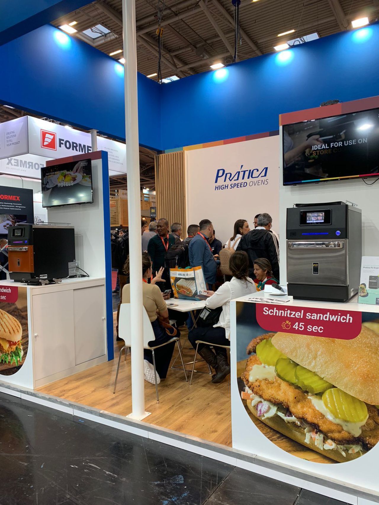 Um grupo de pessoas está sentado em mesas em frente a uma exposição de sanduíches.