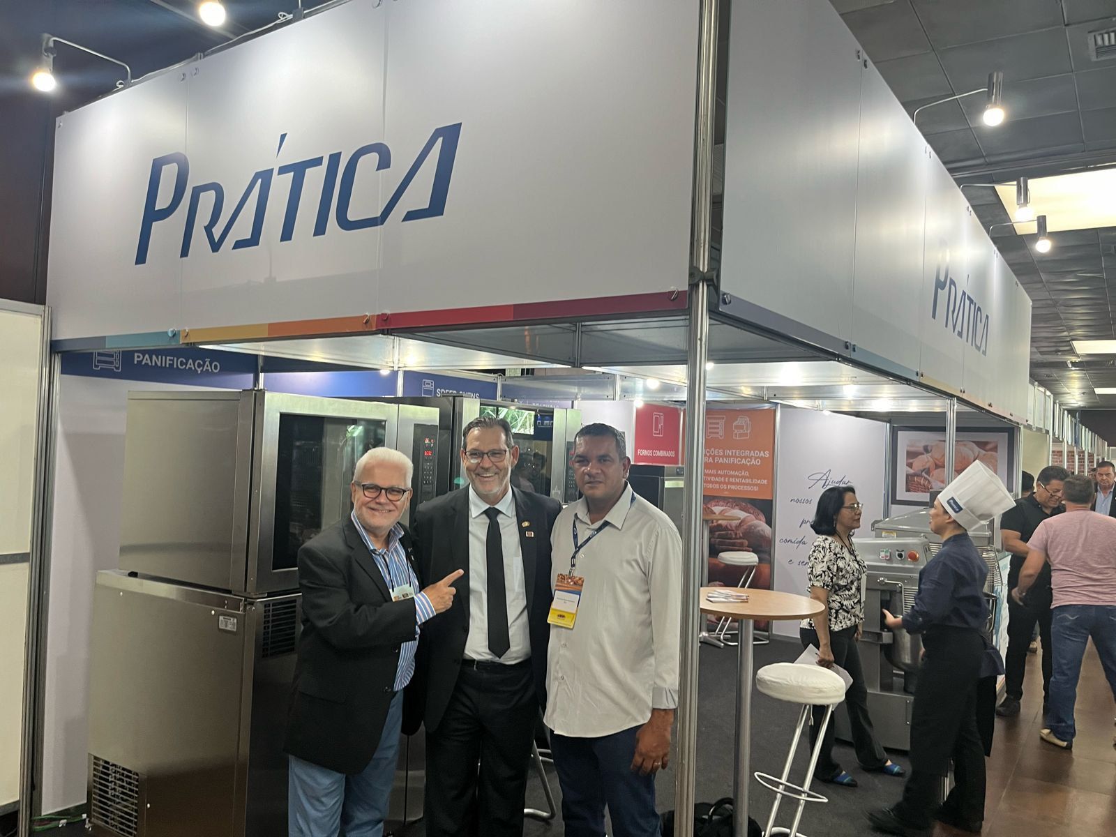 Três homens estão posando para uma foto em frente a um estande em uma convenção.