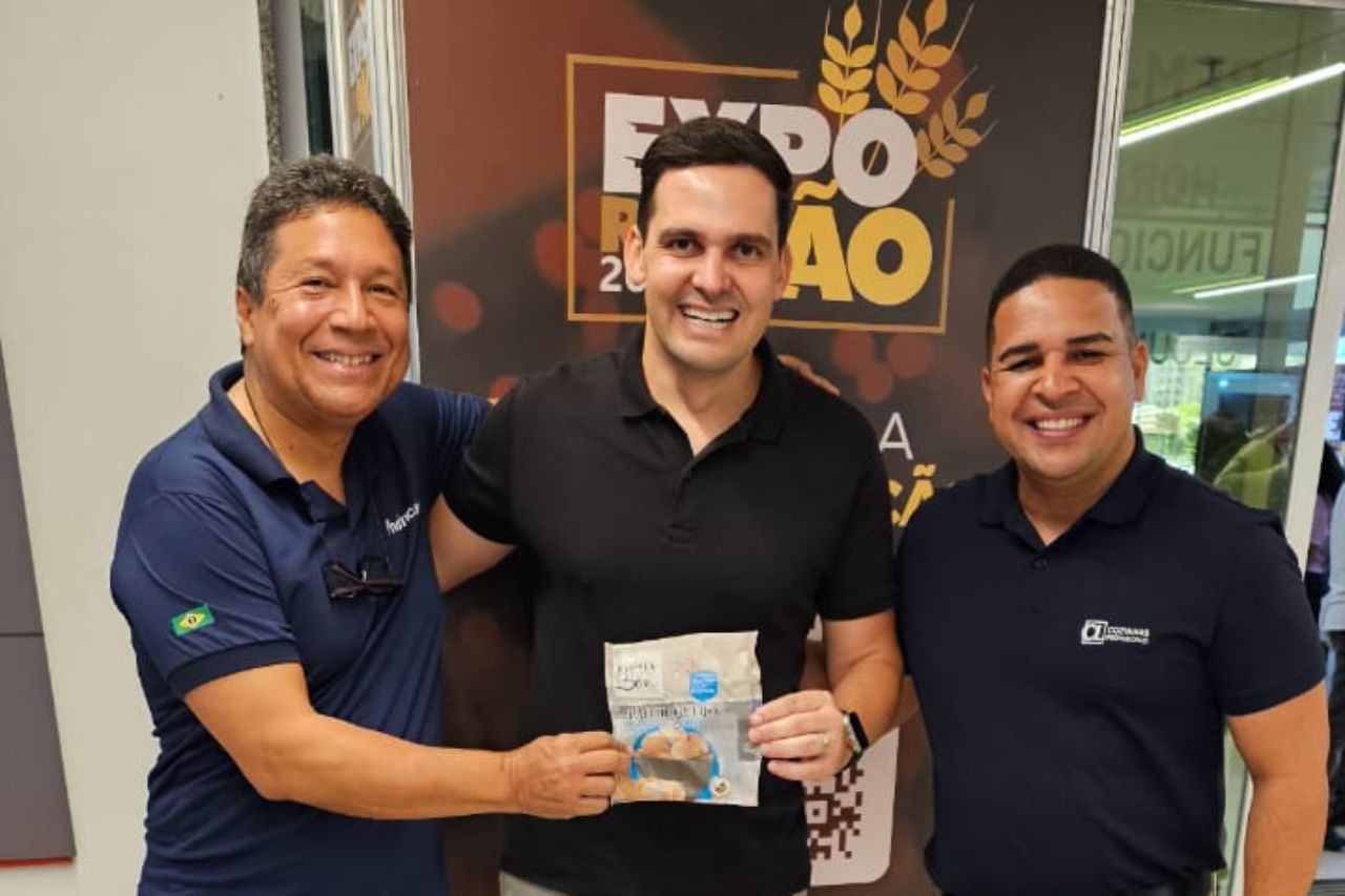 Três homens estão posando para uma foto em frente a uma placa que diz expo