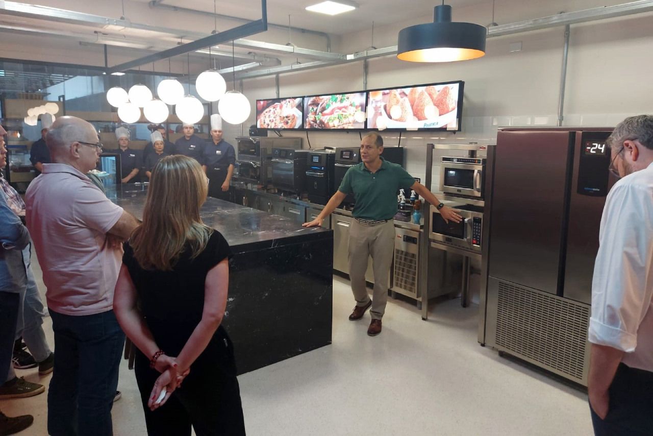 Um homem está conversando com um grupo de pessoas em uma cozinha.