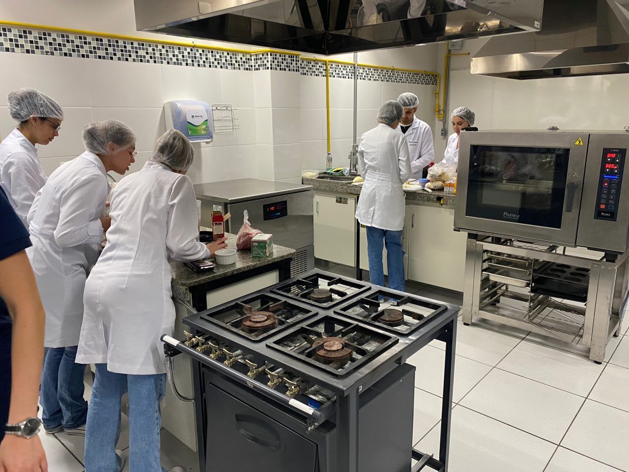 Um grupo de pessoas está em pé ao redor de um fogão em uma cozinha.