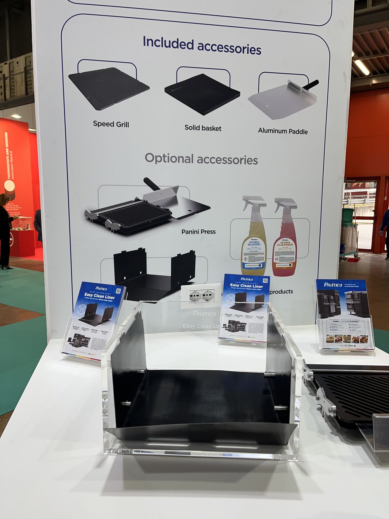 Exposição de acessórios para grelha, incluindo placas de cozimento, produtos de limpeza e uma base de metal, em uma feira comercial.