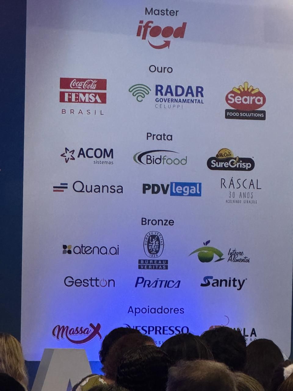 Um grupo de pessoas sentadas em frente a uma parede que diz master ifood