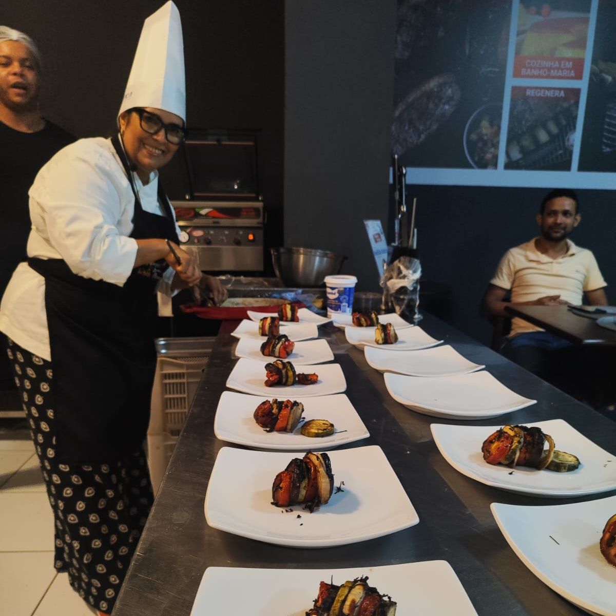Uma mulher com chapéu de chef prepara comida em uma mesa