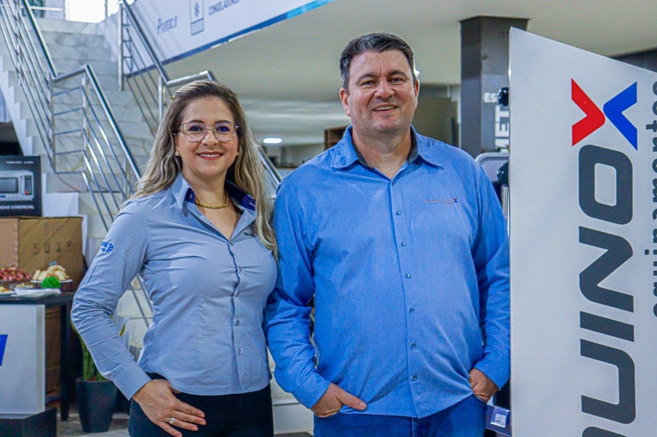 Um homem e uma mulher estão parados um ao lado do outro em frente a uma placa.