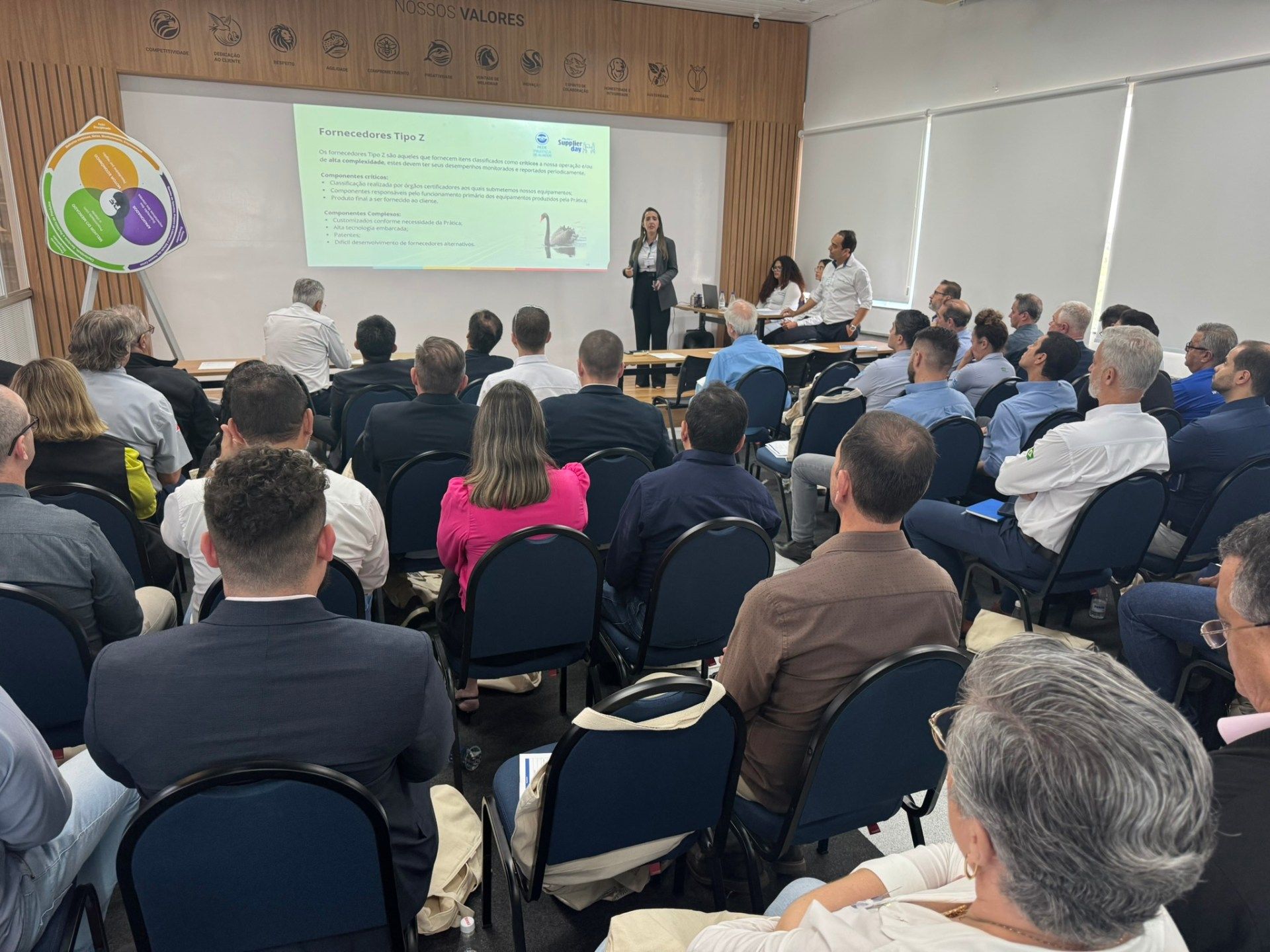 Um grupo de pessoas está sentado em cadeiras em frente a uma tela de projetor.
