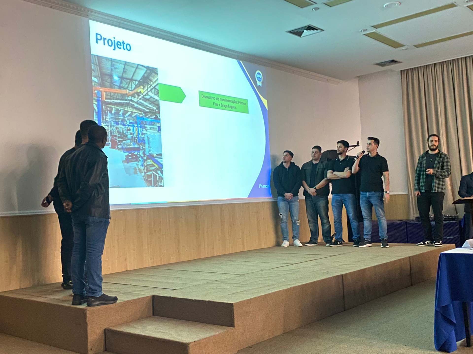 Um grupo de pessoas está em pé em um palco em frente a uma tela grande.