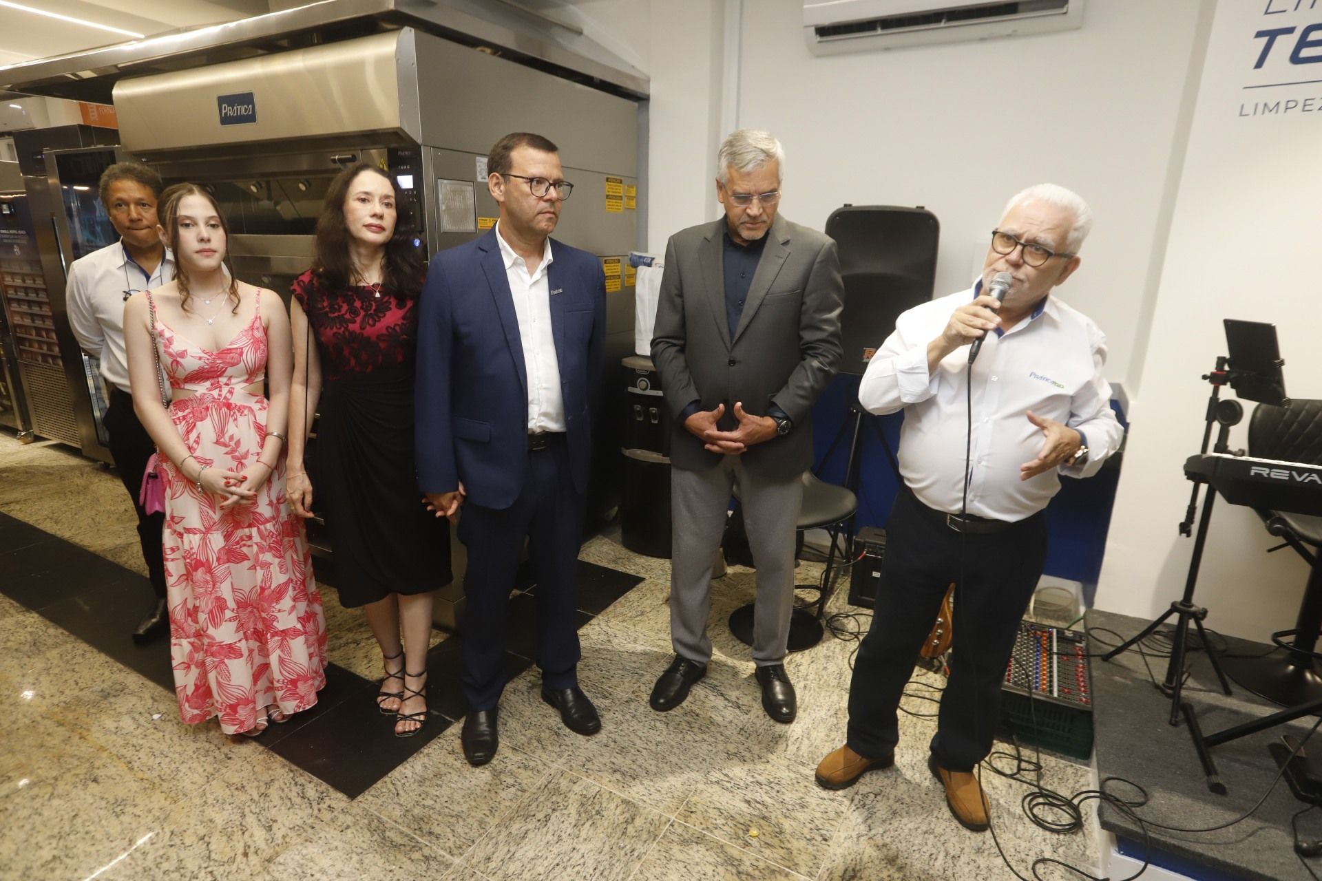 Grupo de pessoas em um evento; homem falando ao microfone. Ambiente de negócios.