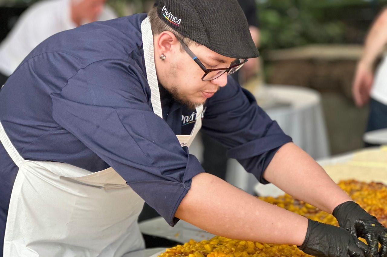 Chef de uniforme e boné azuis empratando comida com luvas pretas.