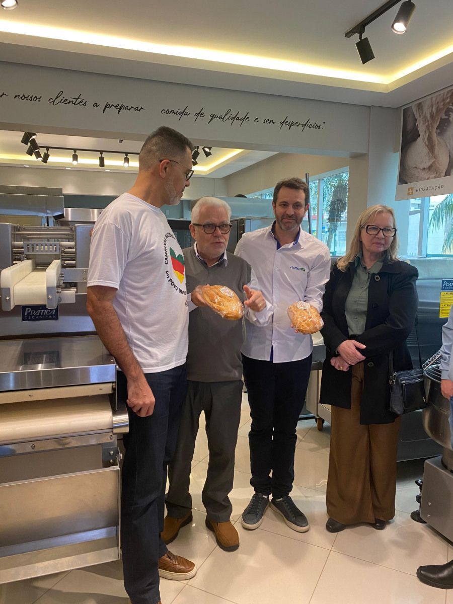 Um grupo de pessoas está de pé, uma ao lado da outra, em uma cozinha, segurando pão.
