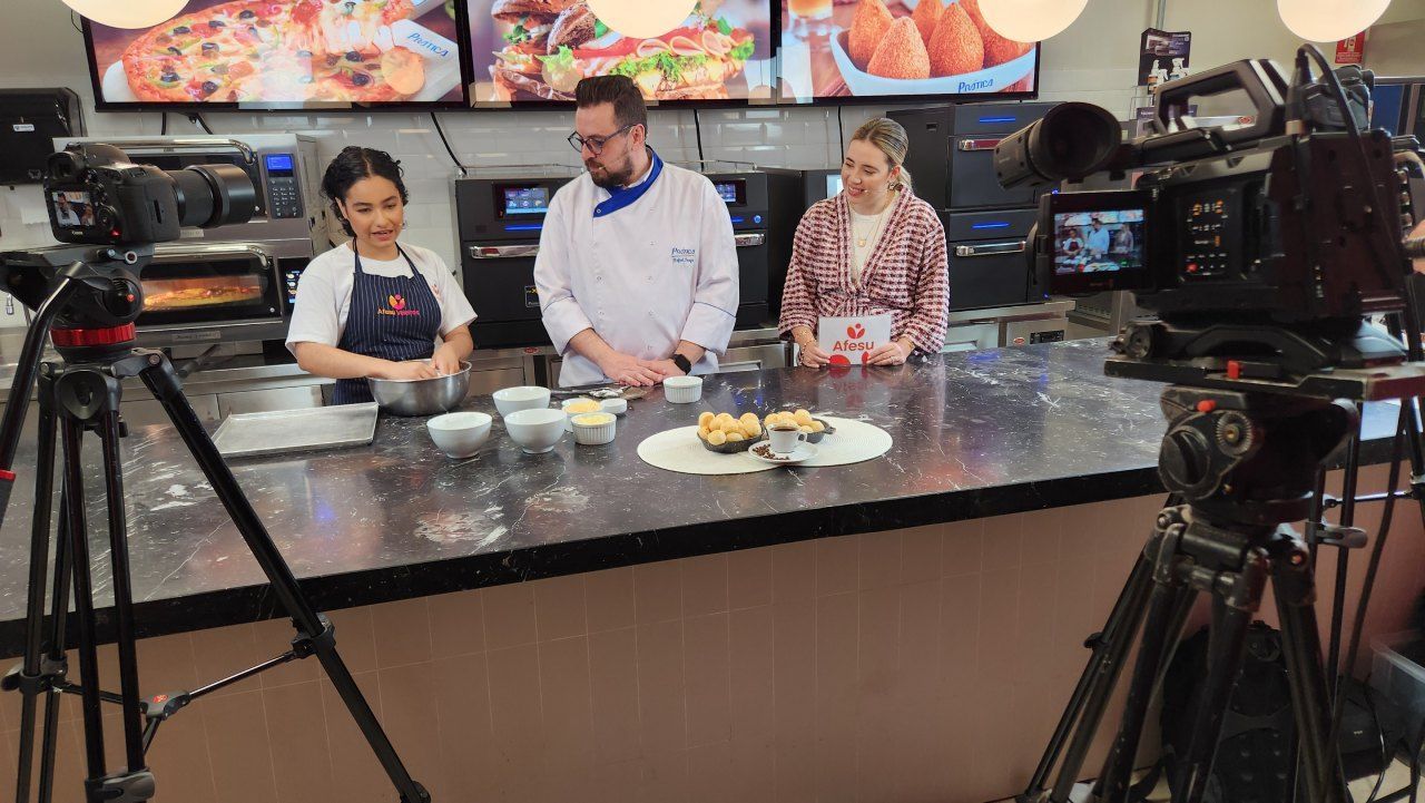 Um grupo de pessoas está em pé ao redor de uma mesa em frente a uma câmera.
