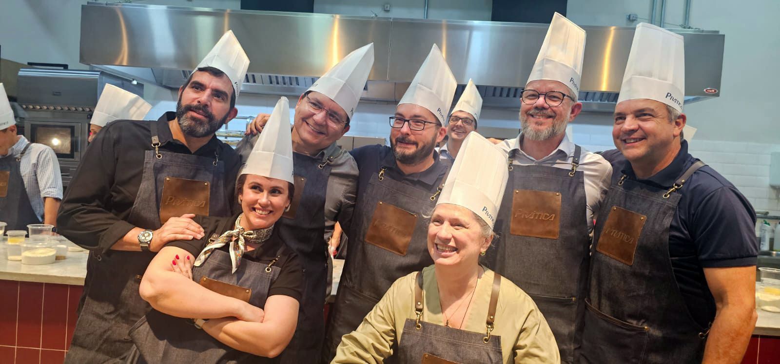 Um grupo de pessoas usando chapéus e aventais de chef estão posando para uma foto em uma cozinha.
