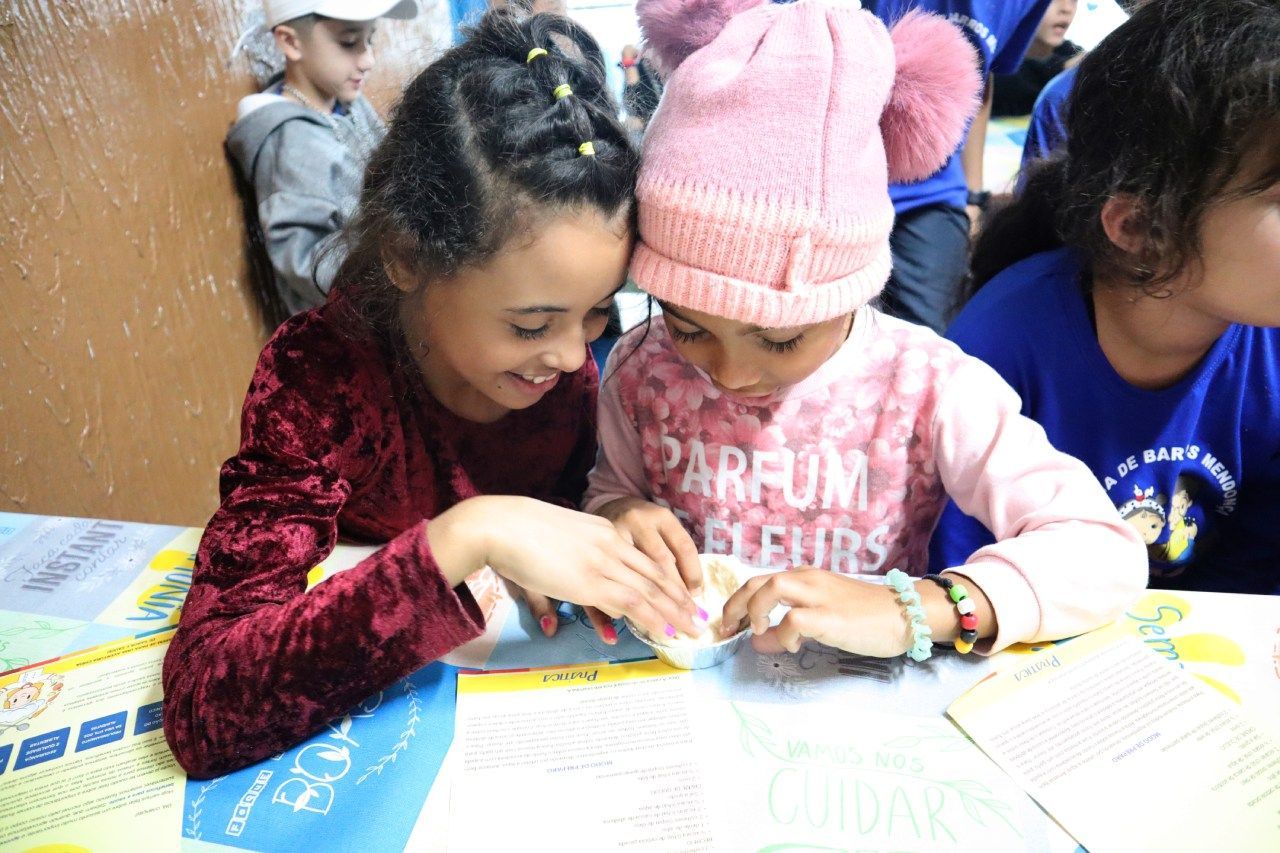 Duas jovens estão sentadas à mesa olhando para um pedaço de papel.