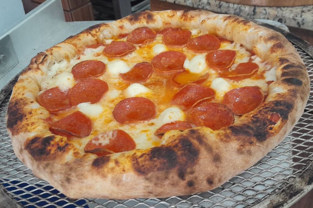 Uma pizza de calabresa está em cima de uma grade de arame.