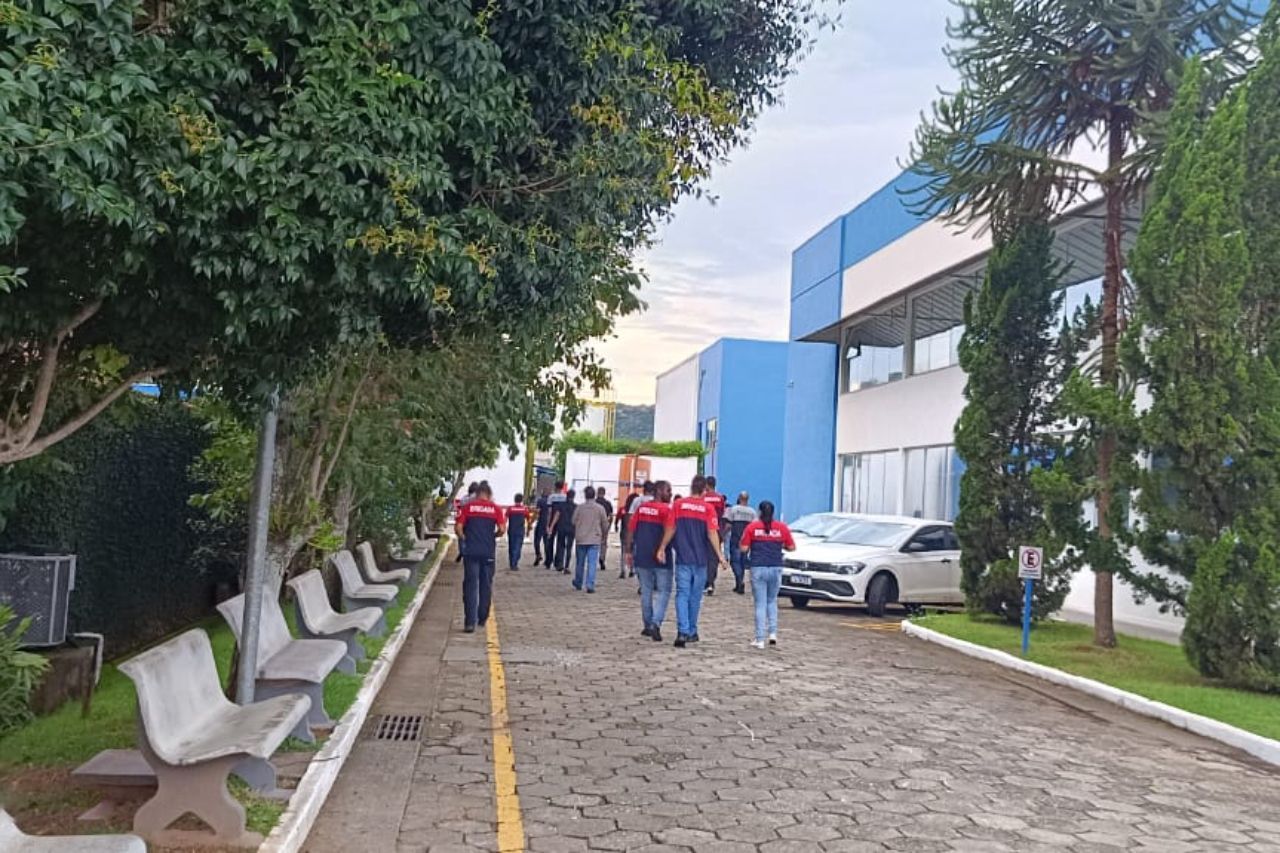 Pessoas com uniformes vermelhos e azuis caminham por uma trilha pavimentada em direção a um prédio azul.